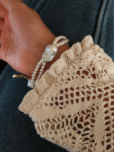 A lifestyle shot of a woman wearing the Isla layered pearl bracelet, showcasing the intricate seed pearl and baroque pearl design against a delicate lace sleeve.