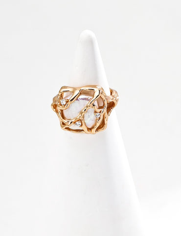 Vera Lustre "Terra" statement ring featuring a large baroque pearl encased in a woven 18K gold vermeil cage, displayed on a white conical ring stand.