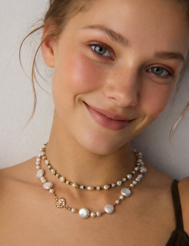 A lifestyle shot showcasing the Cressida baroque pearl necklace resting elegantly on a model's collarbone. The image highlights the CZ-pave detail and the creamy luster of the pearls, demonstrating its ability to transform a minimalist outfit into a high-fashion statement.