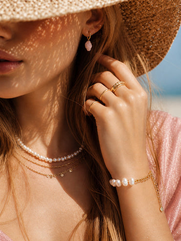 A lifestyle shot of the Astraea pearl link bracelet styled on a model's wrist, showcasing its delicate scale and how the 18K gold accents complement a warm skin tone.