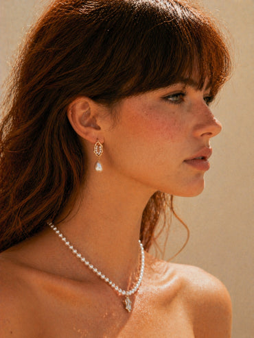 A lifestyle shot of the Selene baroque pearl earrings worn by a model. The visual demonstrates the elegant drop length and how the 18K gold finish complements the pearl's natural glow, showcasing a sophisticated look for modern bridal or daily luxury styling.