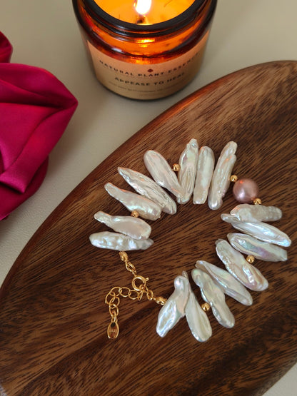 Vera Lustre handcrafted baroque stick pearl bracelet with 18K gold clasp displayed on a wooden tray with a glass candle.