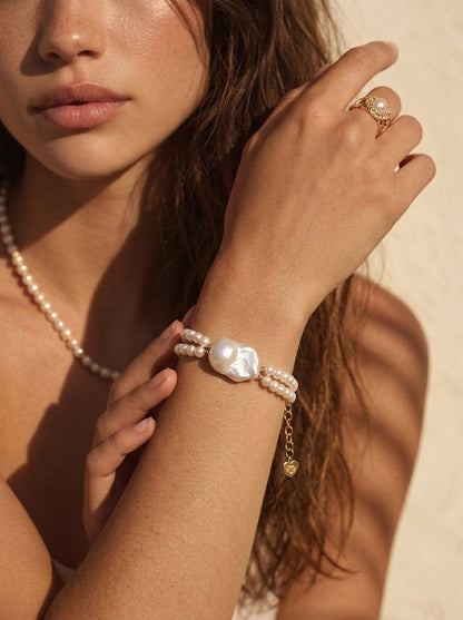A lifestyle shot of a woman wearing the Isla layered pearl bracelet, showcasing the intricate seed pearl and baroque pearl design against a delicate lace sleeve.