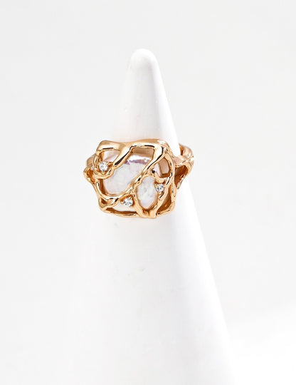Vera Lustre "Terra" statement ring featuring a large baroque pearl encased in a woven 18K gold vermeil cage, displayed on a white conical ring stand.