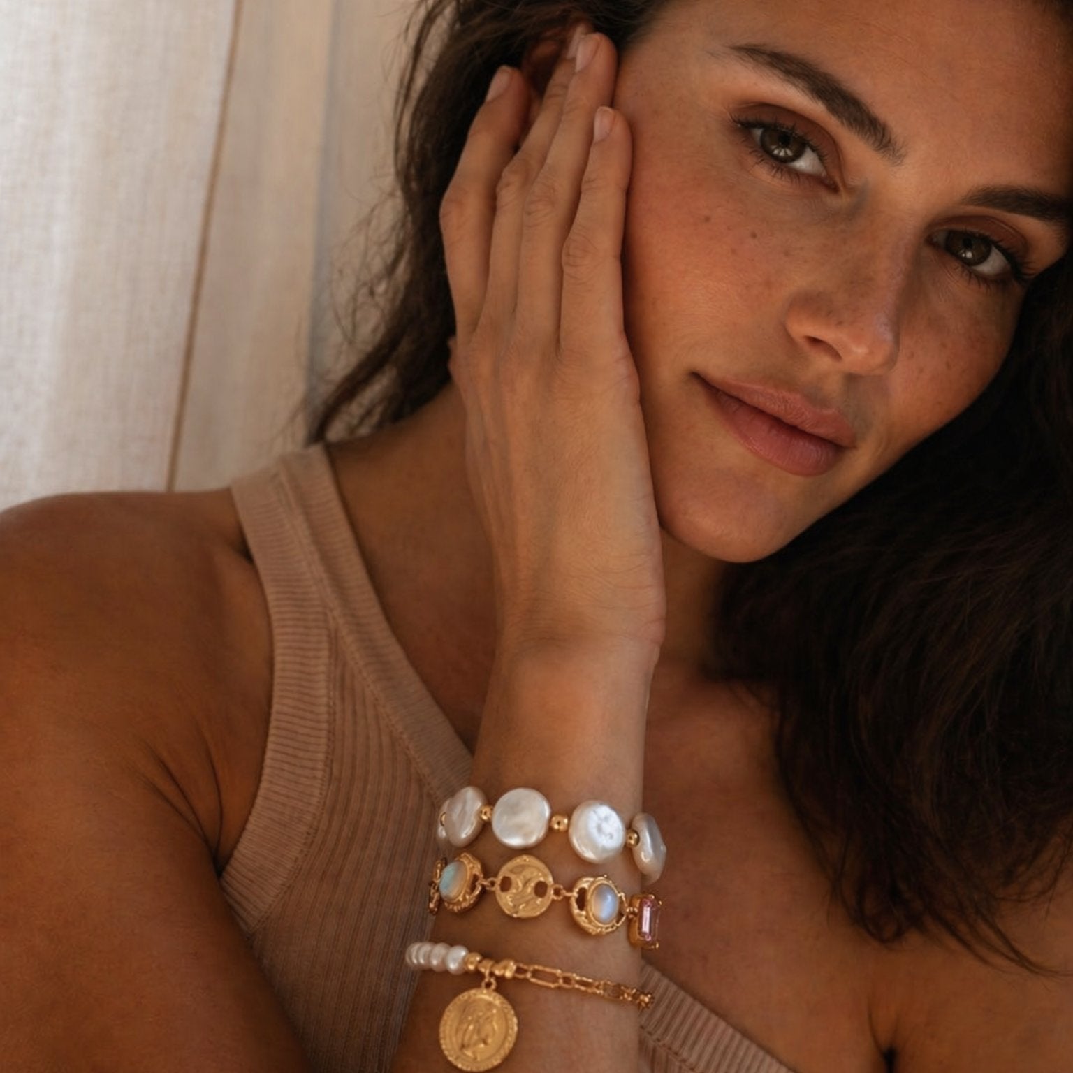 Close-up of a woman wearing layered freshwater pearl and gold bracelets, highlighted by warm natural light, showcasing elegant luxury jewelry