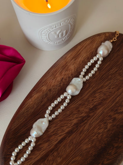 The Vera Lustre Isla dual-layer baroque and seed pearl bracelet elegantly displayed on a warm wooden tray, highlighting its textural complexity.