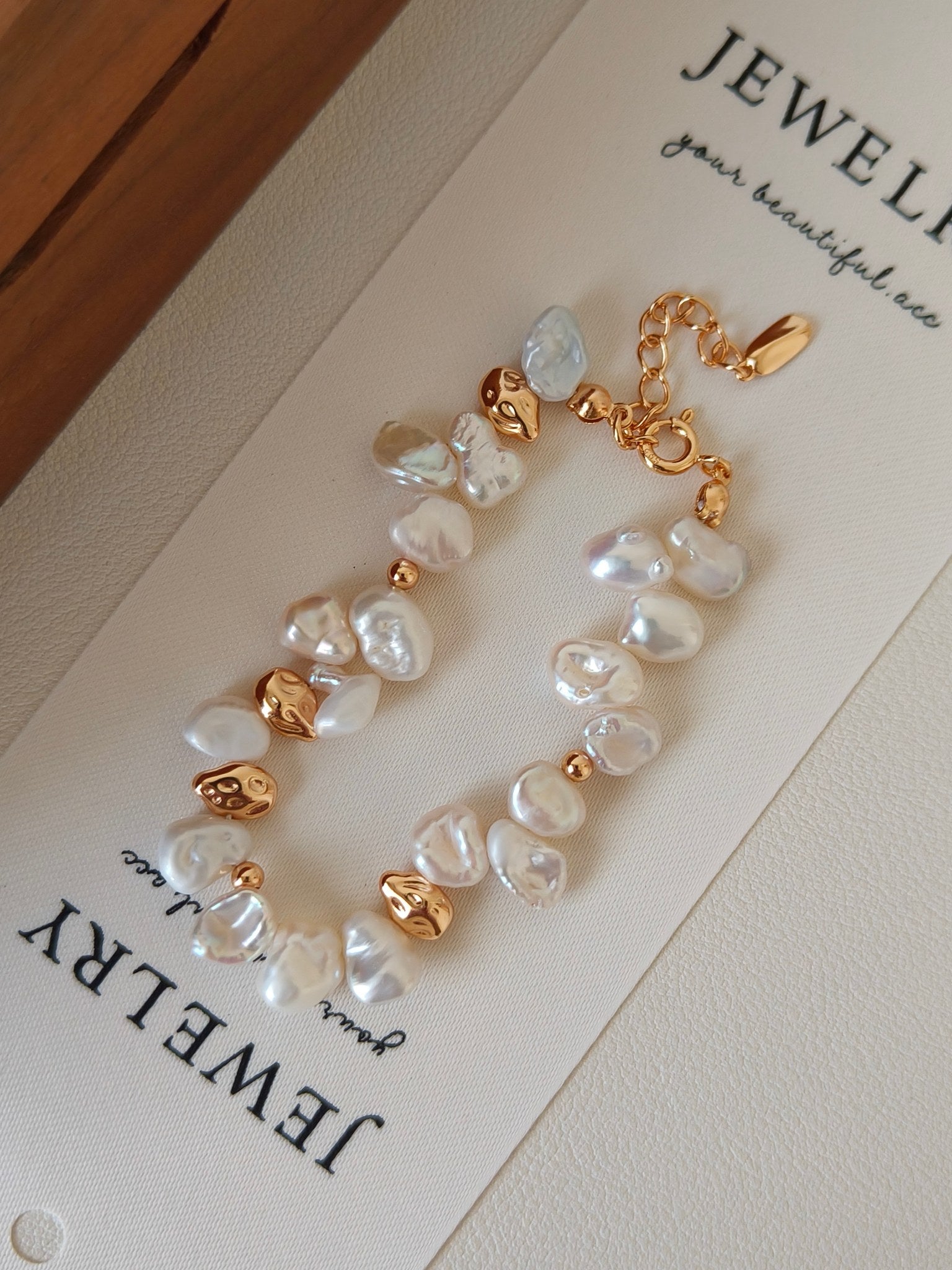 Detailed view of the organic gold nuggets and high-lustre baroque pearls of the Ember bracelet against a Vera Lustre jewelry display card.