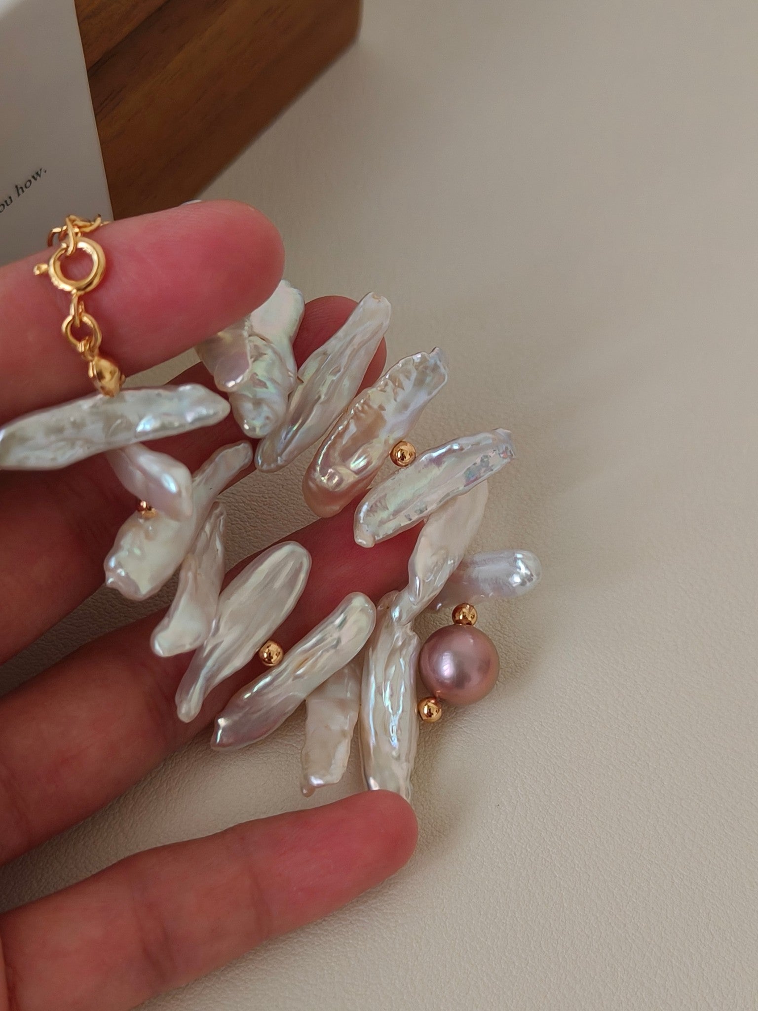 Vera Lustre handcrafted baroque stick pearl bracelet with 18K gold clasp displayed on a wooden tray with a glass candle.