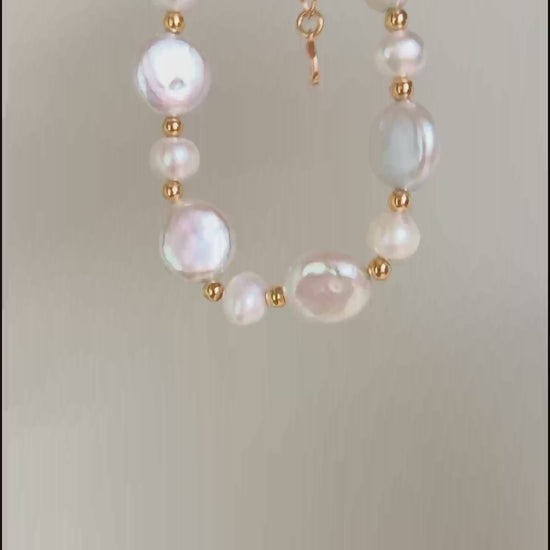 A cinematic video of the Theia bracelet in natural light. The footage captures the shifting iridescence of the baroque pearl and the flickering metallic glow of the golden links as the wrist moves.