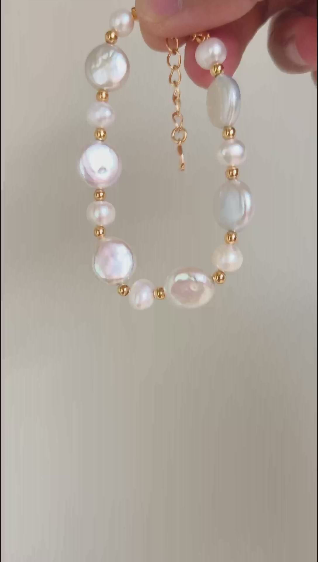 A cinematic video of the Theia bracelet in natural light. The footage captures the shifting iridescence of the baroque pearl and the flickering metallic glow of the golden links as the wrist moves.