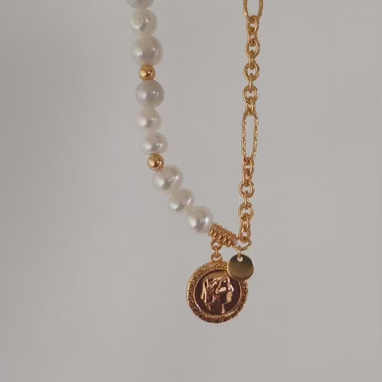This cinematic close-up video captures the dynamic movement and radiant light of the Calyx asymmetric necklace. The camera pans across the soft, iridescent surfaces of natural baroque pearls, transitioning seamlessly into the high-luster glow of the 18K gold vermeil link chain. The video highlights the intricate relief of the vintage Queen Elizabeth coin pendant, showcasing its artisanal texture as it catches the light. This visual demonstration emphasizes the piece's elegant drape and "half-sweet, half-bol