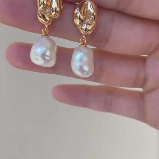 A cinematic video showing the Odyssey earrings in motion. The footage captures the shifting rainbow "orient" of the Mother-of-Pearl against the high-relief golden curves, demonstrating their dynamic, light-catching presence.