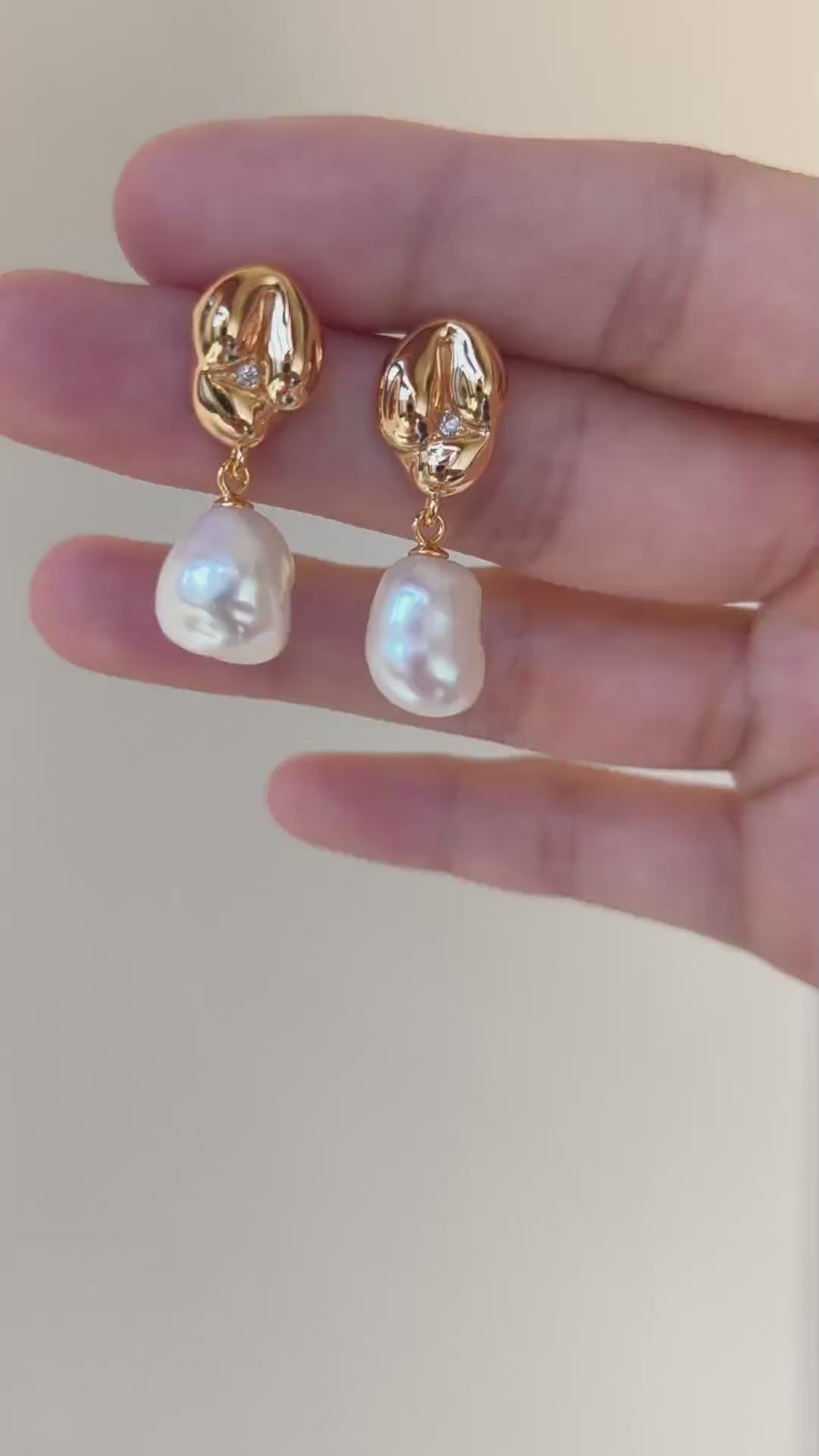 A cinematic video showing the Odyssey earrings in motion. The footage captures the shifting rainbow "orient" of the Mother-of-Pearl against the high-relief golden curves, demonstrating their dynamic, light-catching presence.