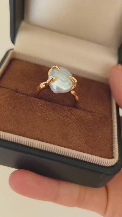A detailed view of the Aura ring being held, demonstrating the mesmerizing glow of the baroque pearl and the comfort of the adjustable open-band design.