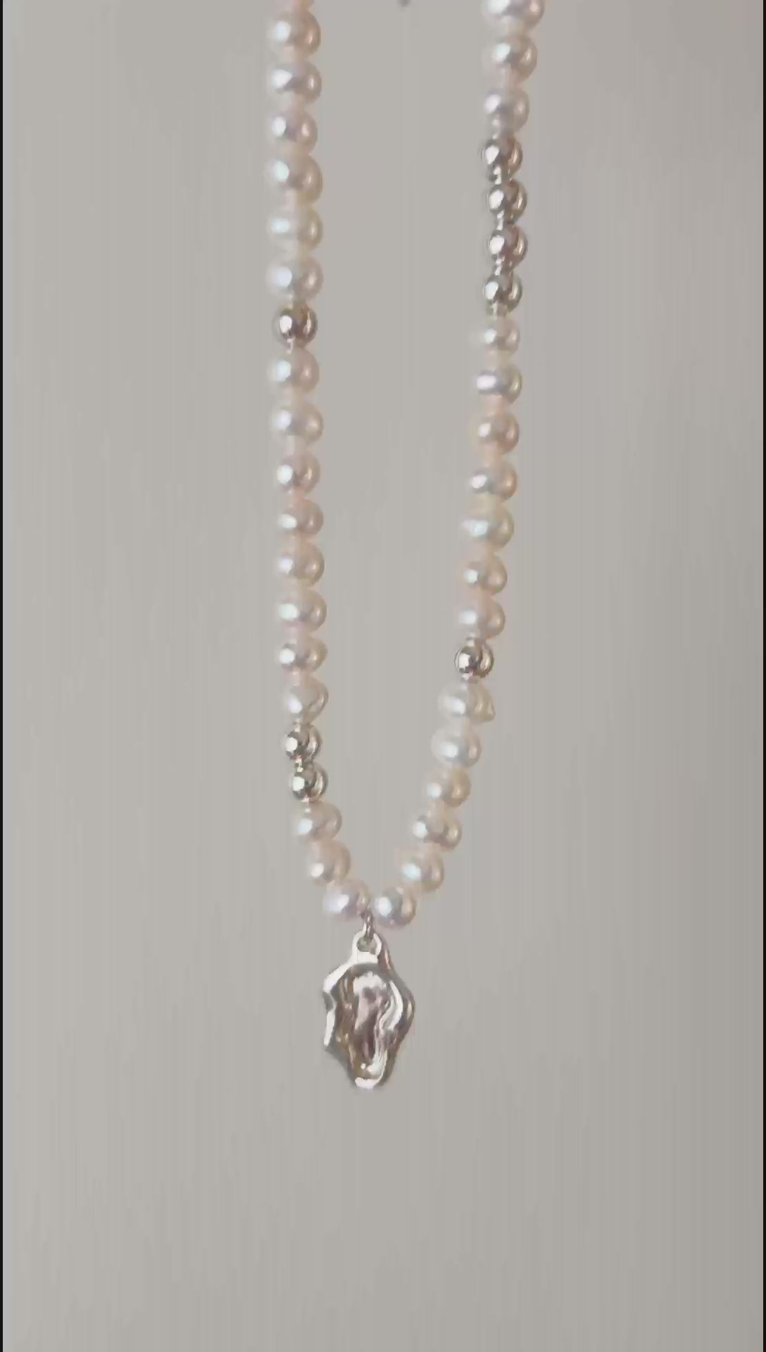 This cinematic close-up video captures the Serene necklace in motion, showing light dancing across the fluid lake medallion. The movement emphasizes the iridescent luster of the 5-5.5mm pearls and the high-shine polish of the silver hardware, illustrating the piece's vivid quality.