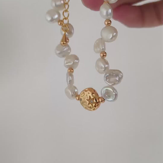 A cinematic product video capturing the shimmering iridescence of the baroque pearls and the flickering metallic light of the gold links in motion.