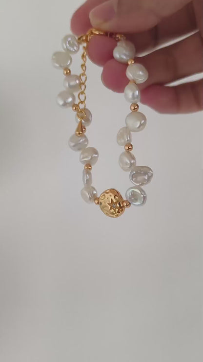 A cinematic product video capturing the shimmering iridescence of the baroque pearls and the flickering metallic light of the gold links in motion.
