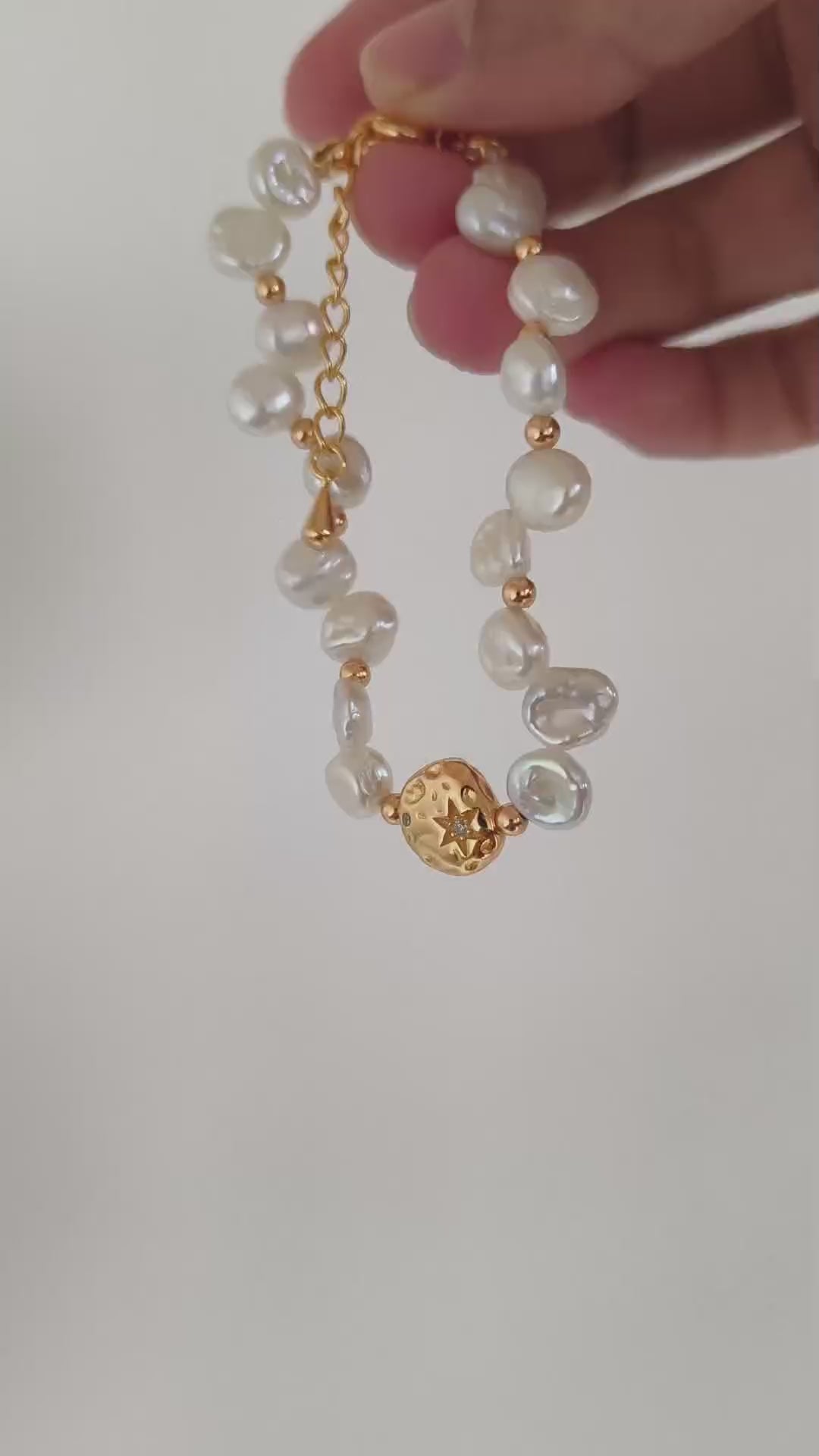 A cinematic product video capturing the shimmering iridescence of the baroque pearls and the flickering metallic light of the gold links in motion.