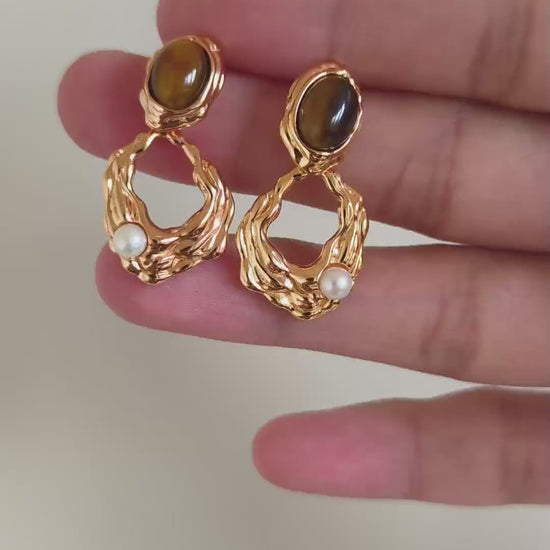 A cinematic video showing the Gaia earrings in motion. The footage captures the shifting golden bands within the Tiger's Eye and the soft iridescence of the pearls as they sway, demonstrating their dynamic elegance.