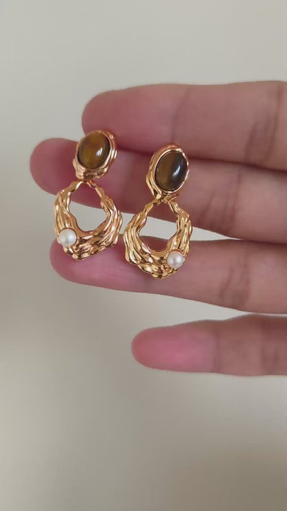 A cinematic video showing the Gaia earrings in motion. The footage captures the shifting golden bands within the Tiger's Eye and the soft iridescence of the pearls as they sway, demonstrating their dynamic elegance.