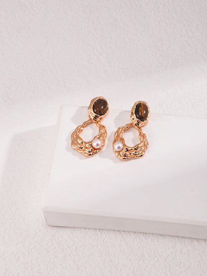 A professional studio shot of the Gaia earrings, showcasing the high-contrast beauty of the 6mm Tiger's Eye and the 4mm freshwater pearl. This image highlights the S925 silver vintage gold craftsmanship.