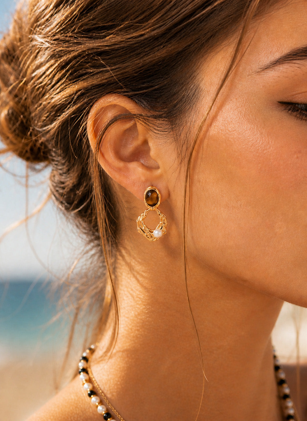 A lifestyle shot of the Gaia Tiger's Eye and pearl earrings styled for a modern bohemian look. The visual demonstrates the 38mm drop length and how the natural stones catch the light to illuminate the face with warm, earthy tones.