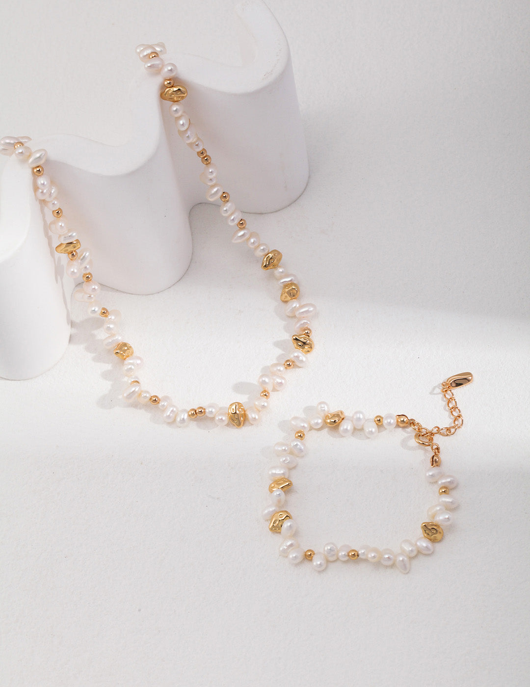 An overhead view of the bracelet and necklace laid flat, showing the rhythmic alternation between the lustrous pearls and the vintage gold hardware.