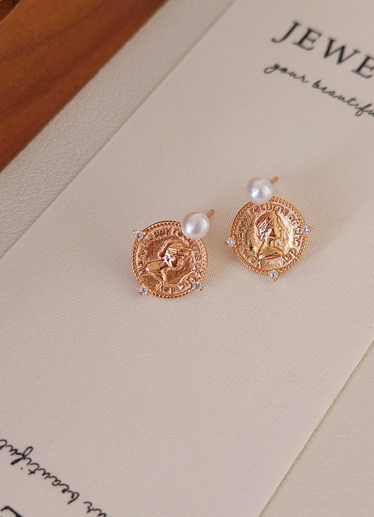 A still-life shot of the coin and pearl earrings placed on an antique tray. This visual reinforces the "Old World Luxury" brand story and highlights the authentic natural materials.
