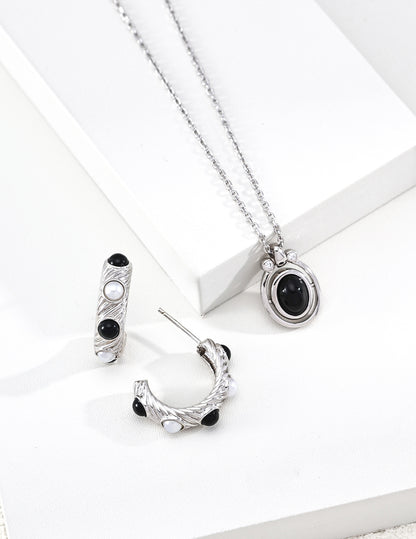A crisp close-up focusing on the Black Agate variant of the Astra necklace. The deep, obsidian hue of the stone is contrasted by a halo of sparkling cubic zirconia, emphasizing the handcrafted S925 sterling silver base and the premium artisanal finish of the rotating mechanism