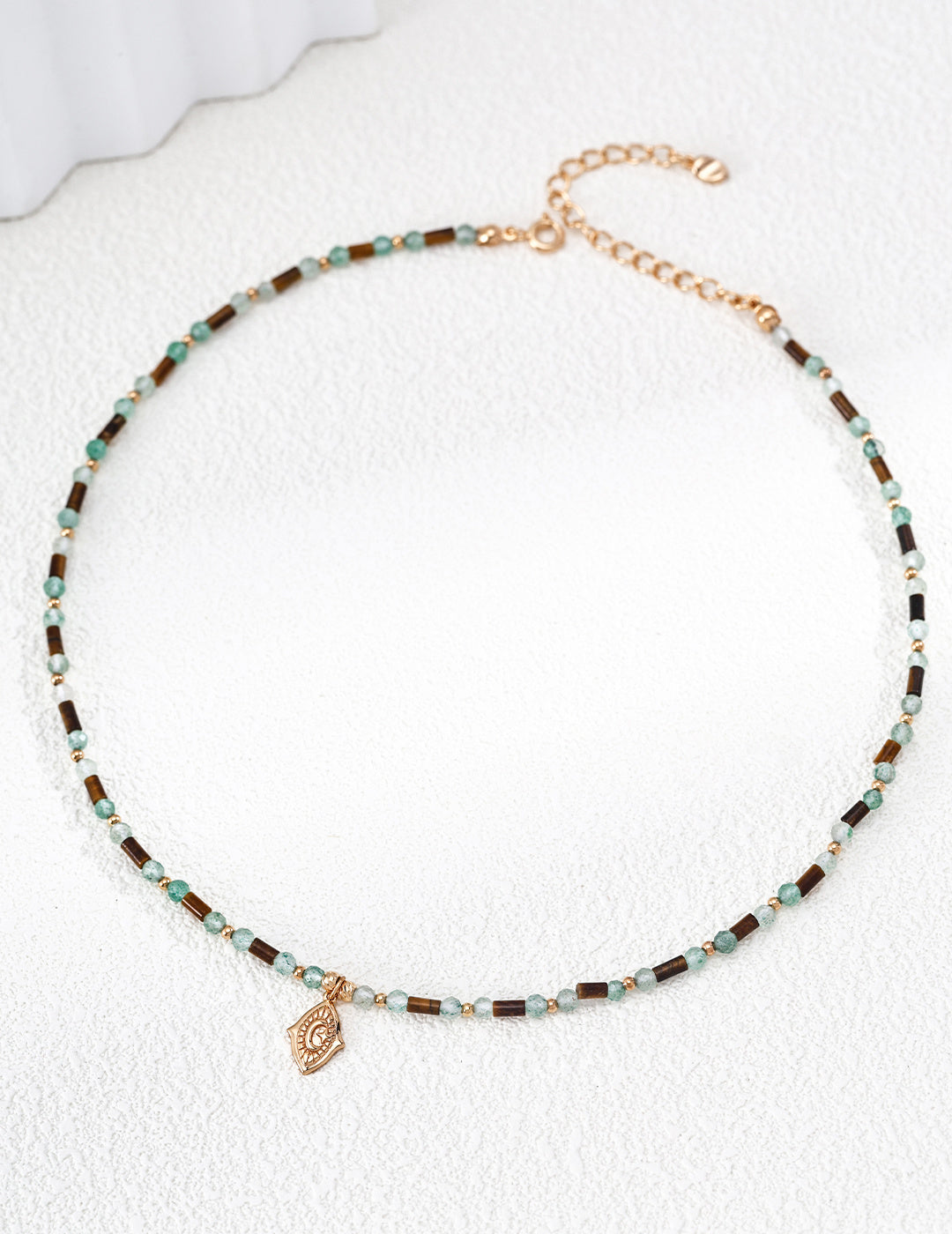 A high-resolution studio shot of the Gaia necklace on a clean surface. This main image clearly displays the rhythmic pattern of 3mm green quartz and sculptural Tiger's Eye stones, emphasizing the handcrafted S925 silver quality and vintage gold finish.