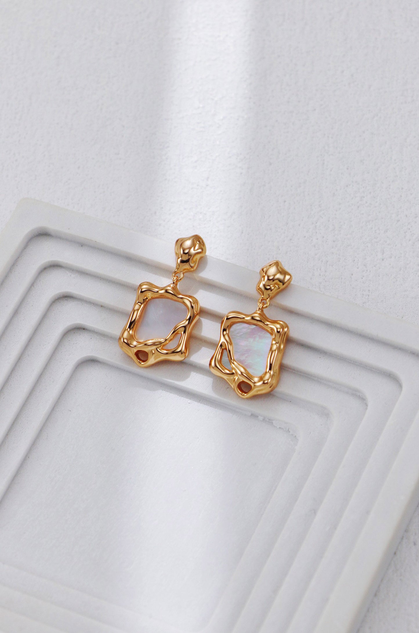 A clean studio shot of the Odyssey earrings, displaying the distorted golden frame and the luminous white shell inlay. This image emphasizes the vintage gold S925 silver quality.