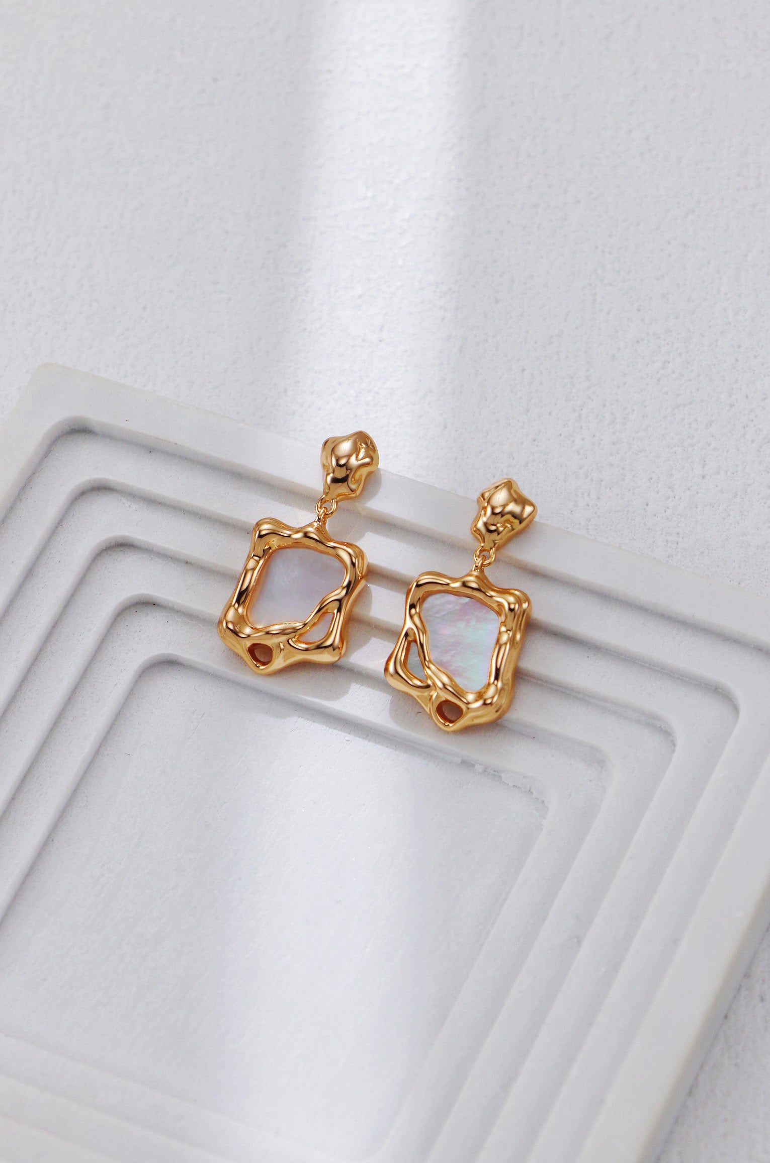 A clean studio shot of the Odyssey earrings, displaying the distorted golden frame and the luminous white shell inlay. This image emphasizes the vintage gold S925 silver quality.