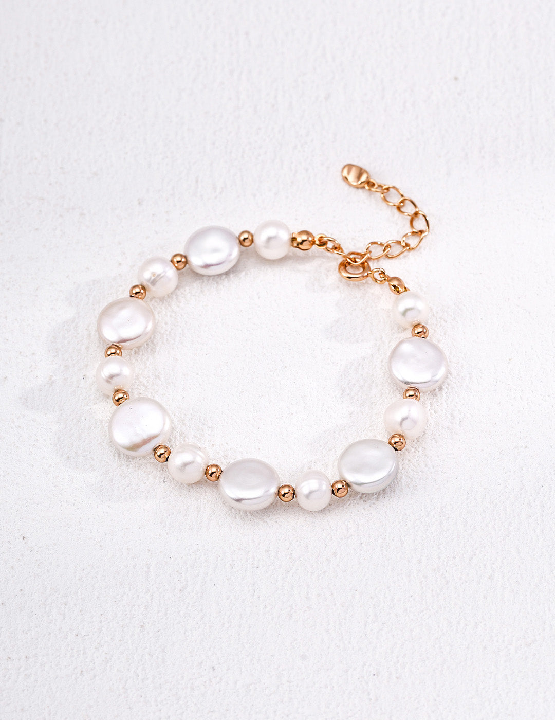 A clean studio shot of the Theia bracelet, showcasing the high-orient luster of the irregular baroque pearl and the alternating golden bead and petite pearl strand.