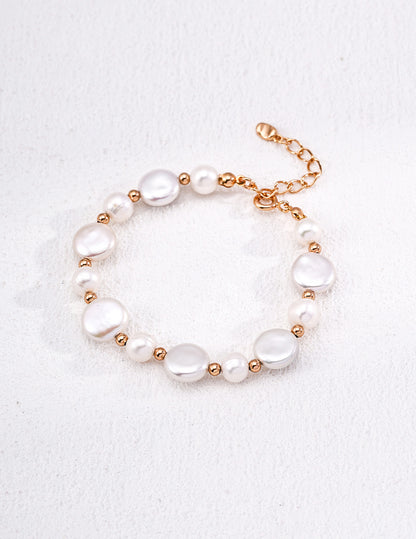 A clean studio shot of the Theia bracelet, showcasing the high-orient luster of the irregular baroque pearl and the alternating golden bead and petite pearl strand.