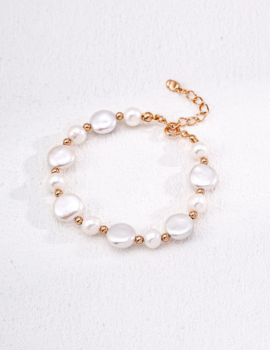 A clean studio shot of the Theia bracelet, showcasing the high-orient luster of the irregular baroque pearl and the alternating golden bead and petite pearl strand.
