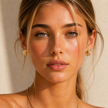 A lifestyle shot of the Kardia heart stud earrings worn by a model. The visual highlights the 1.8cm scale and how the vintage gold finish adds a touch of "effortless edge" to a chic, minimal look.