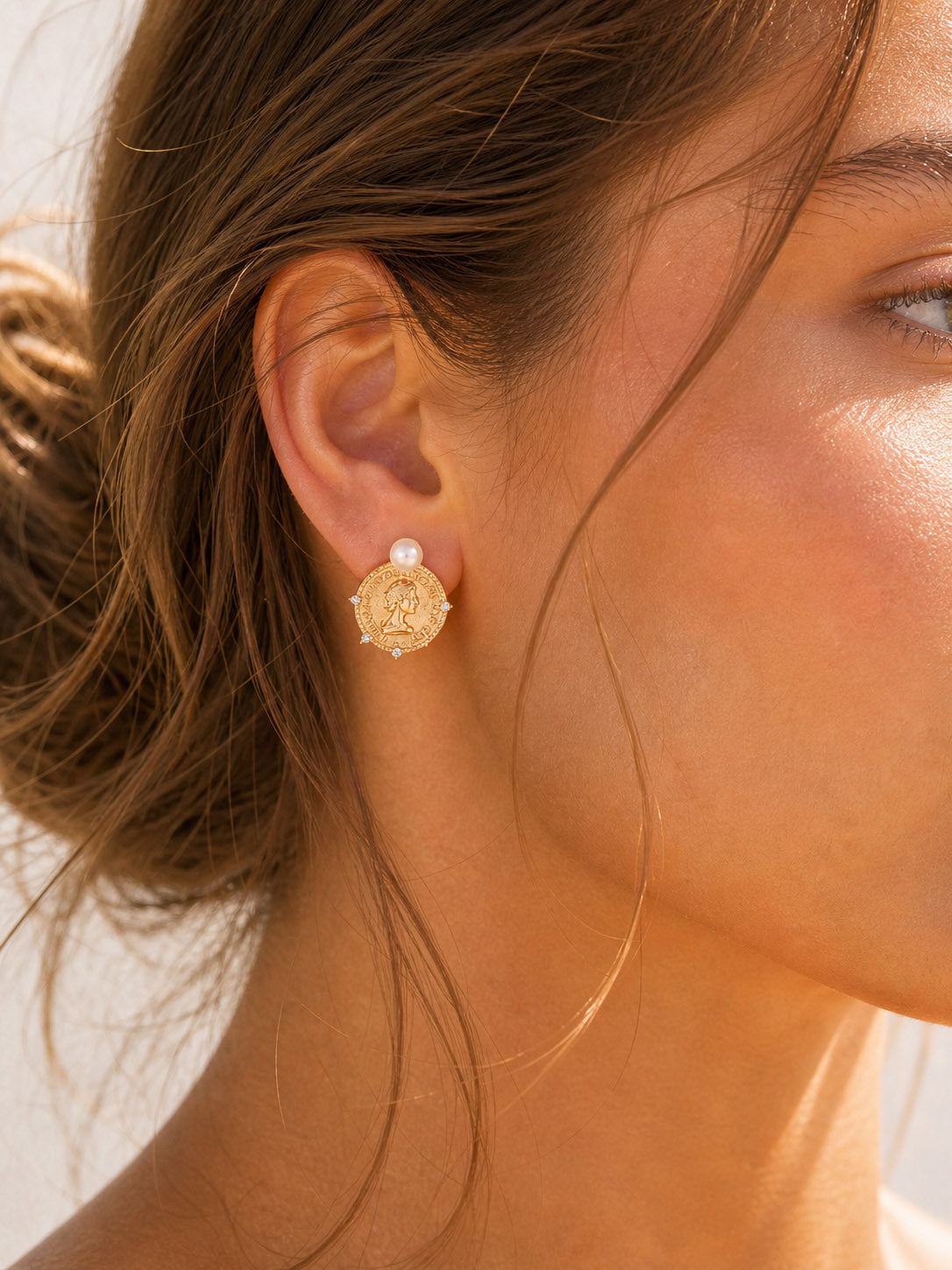 A lifestyle shot of the Aurelia coin pearl earrings styled for an elegant day look. The visual highlights the perfect drop length and how the embossed gold coins catch the light to frame the face with vintage warmth.