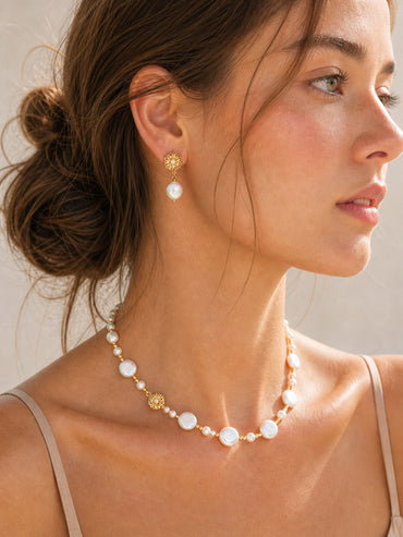 A lifestyle shot of the Soleil sunflower pearl earrings worn by a model. The visual demonstrates the elegant 3.2cm drop length and how the sparkling CZ stones catch the light to illuminate the face.