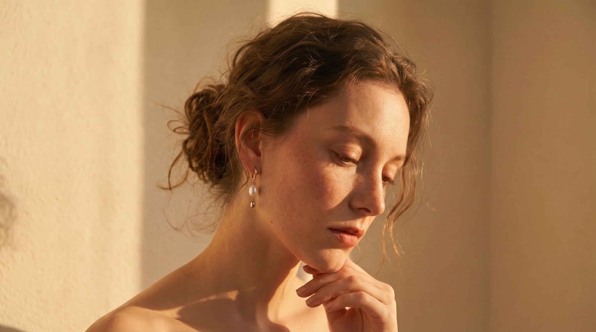 A woman with a soft updo wearing elegant baroque pearl drop hoop earrings, illuminated by warm natural sunset light, representing a quiet luxury aesthetic for handmade jewelry.