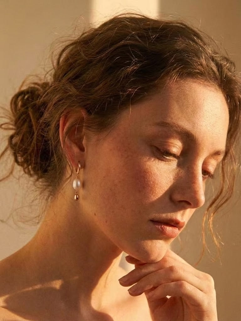 Minimalist baroque pearl drop earrings on a model, warm sunset lighting, chic summer jewelry banner.