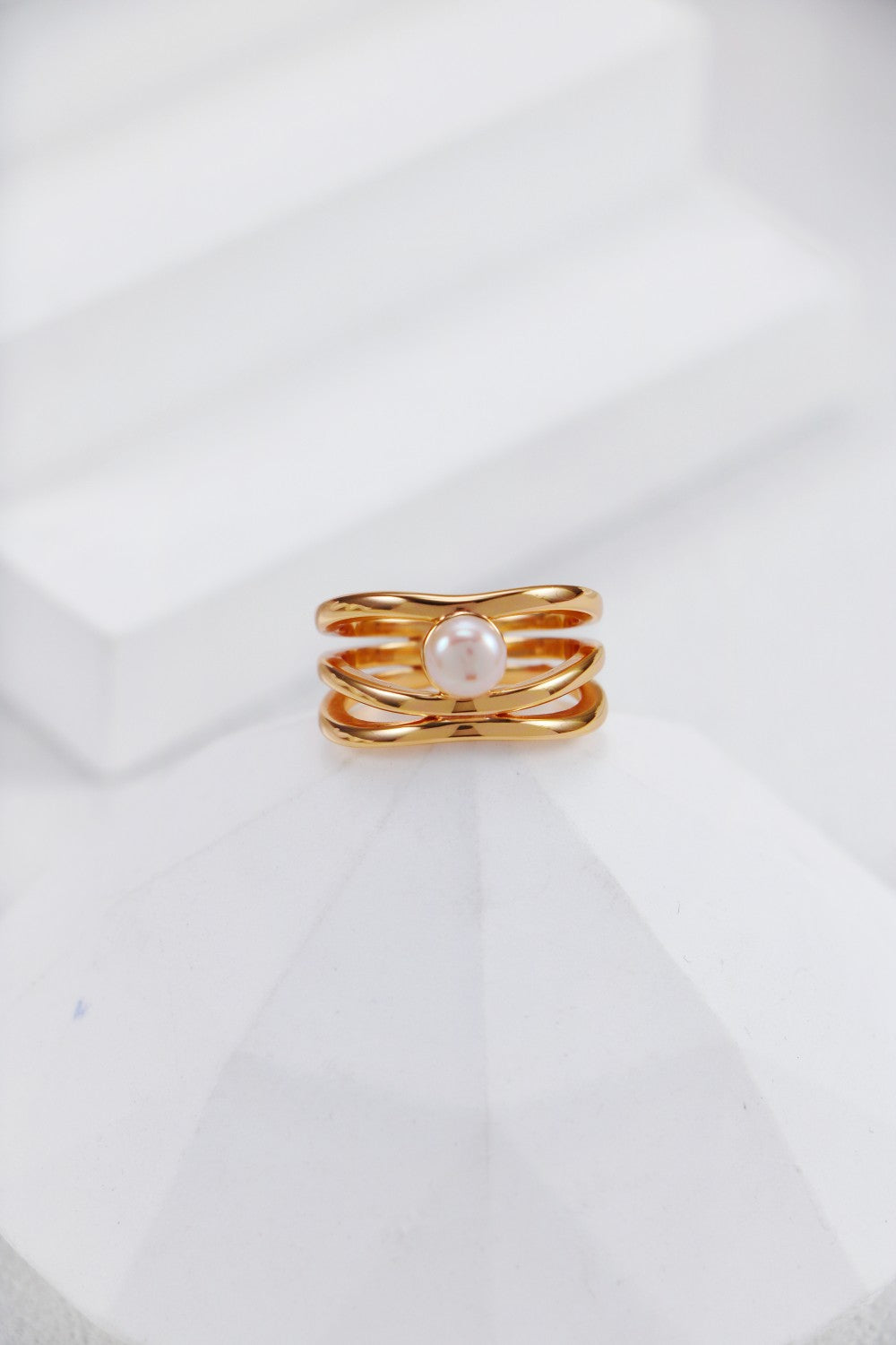 A professional studio shot of the Clara infinity pearl ring in vintage gold, highlighting the intricate interlaced band and the high-orient luster of the central pearl.