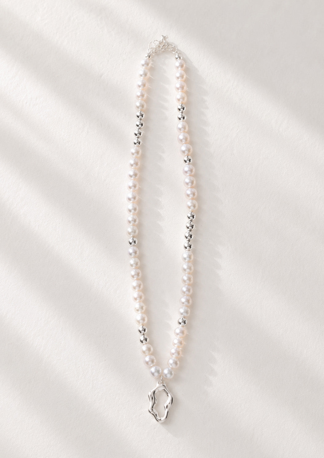 A high-resolution studio shot of the Serene necklace featuring the sculptural silver pendant and a strand of 5mm freshwater pearls. This main image emphasizes the contrast between the mirror-finish silver and the soft pearlescent glow, perfect for customers seeking artisan silver pearl jewelry.