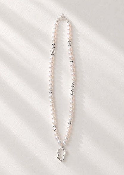 A high-resolution studio shot of the Serene necklace featuring the sculptural silver pendant and a strand of 5mm freshwater pearls. This main image emphasizes the contrast between the mirror-finish silver and the soft pearlescent glow, perfect for customers seeking artisan silver pearl jewelry.