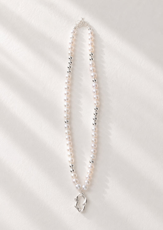 A high-resolution studio shot of the Serene necklace featuring the sculptural silver pendant and a strand of 5mm freshwater pearls. This main image emphasizes the contrast between the mirror-finish silver and the soft pearlescent glow, perfect for customers seeking artisan silver pearl jewelry.